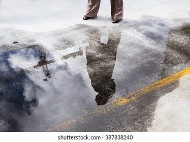 Upward Profile Of A Business Woman Through The Reflection In A Puddle Of Water On The Ground