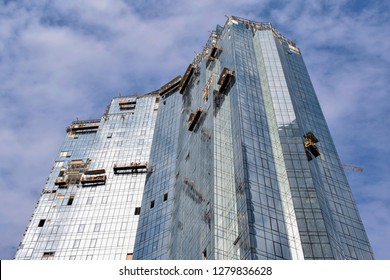 Upward view of a high building with many suspended cradles and workers in them. Suspended cradles with workers working with the facade of a skyscraper.