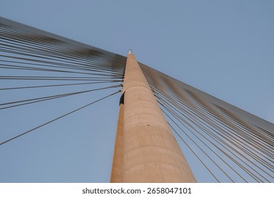 Upward view of modern cable-stayed bridge with geometric lines and clear sky, minimal architectural composition