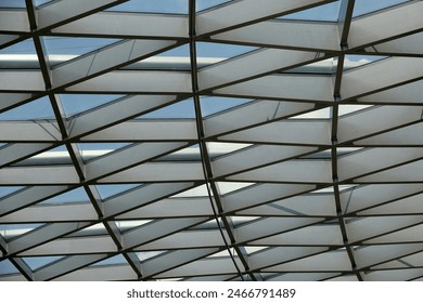 An upward view of a modern geometric glass roof construction, featuring a complex network of triangular panels framing the blue sky. - Powered by Shutterstock