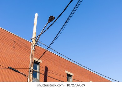 Upward View Of A Wood Power Pole And Street Light Set Against A Red Brick Industrial Building, Blue Sky Copy Space, Horizontal Aspect