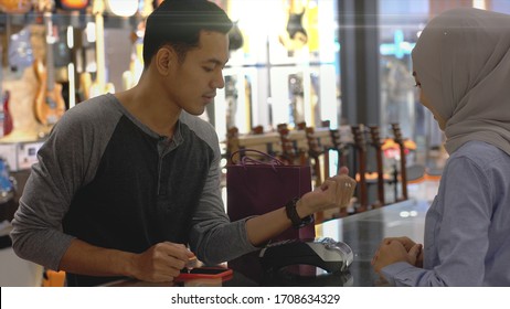 An Upwardly Mobile Asian Muslim Man Using A Mobile Phone - Smartwatch To Pay For A Product At A Sale Terminal With Nfc Identification Payment For Verification And Authentication