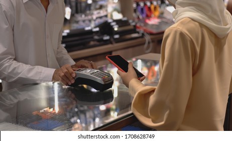 An Upwardly Mobile Asian Muslim Woman Using A Mobile Phone - Smartwatch To Pay For A Product At A Sale Terminal With Nfc Identification Payment For Verification And Authentication