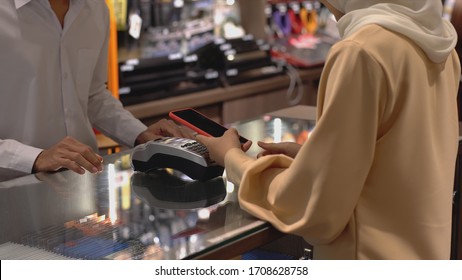 An Upwardly Mobile Asian Muslim Woman Using A Mobile Phone - Smartwatch To Pay For A Product At A Sale Terminal With Nfc Identification Payment For Verification And Authentication