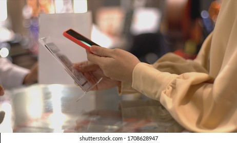 An upwardly mobile Asian Muslim woman using a mobile phone - smartwatch to pay for a product at a sale terminal with nfc identification payment for verification and authentication - Powered by Shutterstock