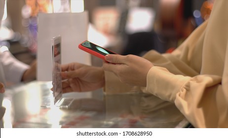 An upwardly mobile Asian Muslim woman using a mobile phone - smartwatch to pay for a product at a sale terminal with nfc identification payment for verification and authentication - Powered by Shutterstock