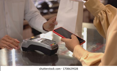 An upwardly mobile Asian Muslim woman using a mobile phone - smartwatch to pay for a product at a sale terminal with nfc identification payment for verification and authentication - Powered by Shutterstock