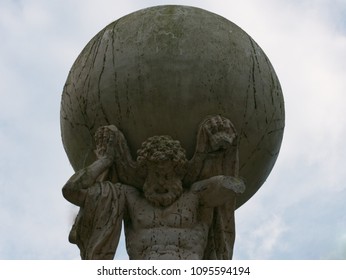 Upwards and frontal view to statue of Atlas carrying the world globe on its shoulders with a slightly clouded blue sky on the background