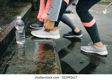 Urban Athletes Lacing Sport Footwear For Running In The City Under The Rain. Two Women Getting Ready For Outdoor Training And Fitness Exercising On Cold Winter Weather.