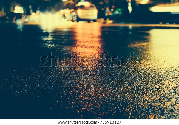 Urban city rainy night, light from the shop\
windows reflected on the road on which fast moving cars. View from\
the level of asphalt