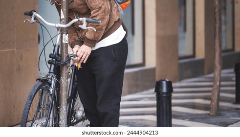 Urban cyclist locking bike to pole, holding keys in hand, amidst city architecture backdrop - Powered by Shutterstock