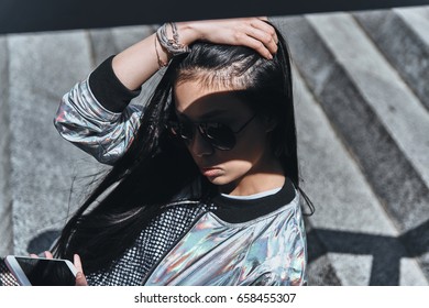 Mujer urbana. Hermosa joven con ropa informal, sosteniéndose de la mano en el pelo mientras está sentada en las escaleras al aire libre