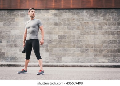 urban fitness man holding kettlebell. Sporty strong male working out outdoors.