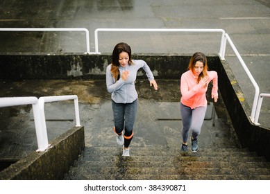 Urban Fitness Women Running And Climbing Stairs For Legs Power And Strength Training. Female Athletes Working Out Outdoor In Rainy Winter Day.