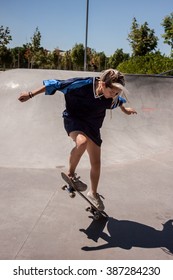 Urban Girl Skating In A Skate Park. The Girl Is Wearing A Big Blue Shirt.