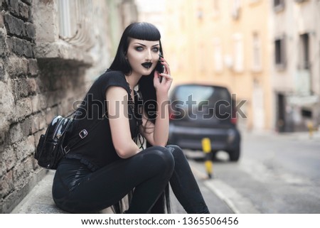 Urban goth girl talking over her cell phone, sitting in an urban outdoor area