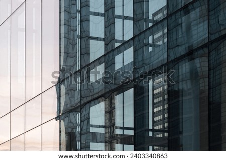 Urban high rise buildings reflected in modern glass skyscraper windows at sunset. Abstract architectural background.