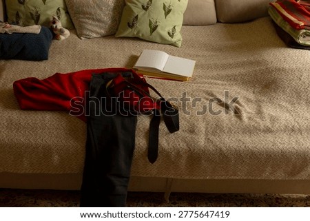 Urban jacket and backpack left on sofa. Open book and scattered throw create narrative of abrupt departure, warm interior tones, textured fabric, hallway glimpse and everyday 