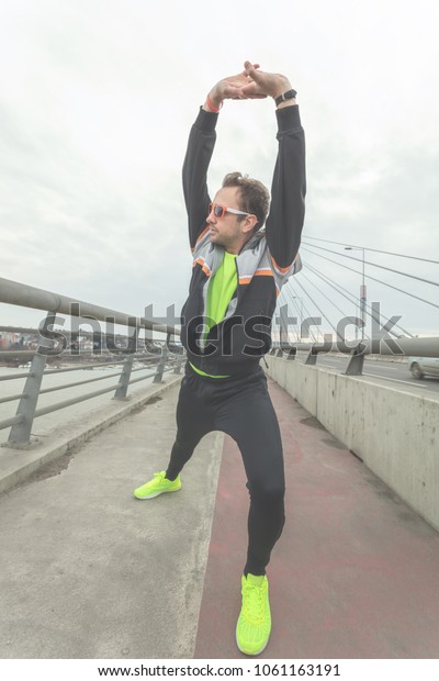 Urban\
jogger stretching on a bridge above the\
river.\
