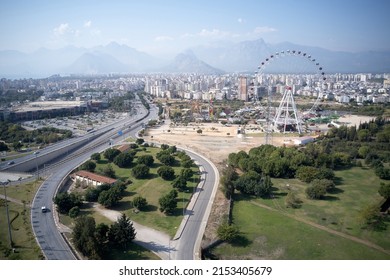 Urban landscape of Antalya town. Panoramic view of city buildings, road, Ferris wheel and mountains in the background.
