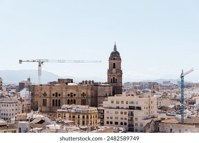 an urban landscape dominated by a large historic building with a dome and bell tower, surrounded by modern residential and commercial buildings. Mountains are visible in the distance, and two construc - Powered by Shutterstock