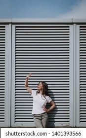 Urban Lifestyle Concept. Waist Up Portrait Of Young Happy Lady In Jeans And T-shirt Leaning On City Building And Covering Sun Shine By Hand