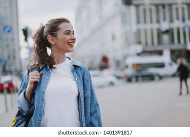 Urban lifestyle concept. Waist up side face portrait of young pretty cheerful lady looking aside while walking around city. Copy space on right