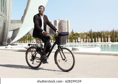 Urban lifestyle, ecology and transportation concept. Fashionable modern ecologically friendly young Afro American businessman wearing trendy round shades and formal suit cycling to work on bicycle - Powered by Shutterstock