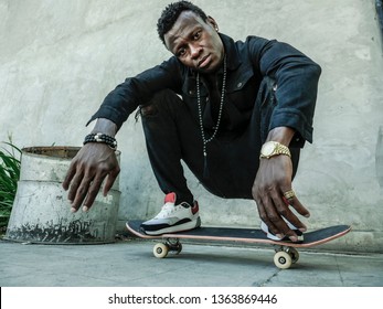 urban lifestyle portrait of young attractive and serious black African American man squatting on skate board at grunge street corner looking cool posing in badass bad boy attitude in city life 