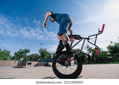 An urban middle-aged man is performing a 360 rotation on one wheel on his bmx in a skate park. A tattooed mature professional bike rider is balancing on on wheel of his bike. - Powered by Shutterstock