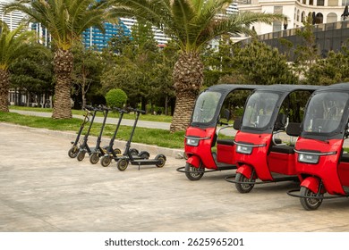 Urban mobility options with row of shared electric scooters and bright red three-wheeled tuk-tuk taxis parked in tourist area. 
