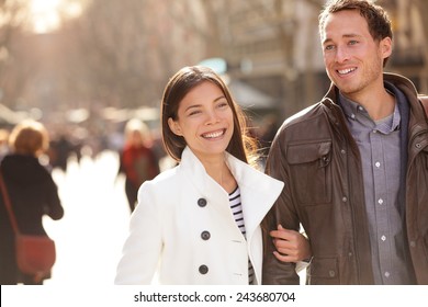 Urban modern young professionals couple walking romantic laughing talking holding hands on date. Young multicultural couple Asian and Caucasian on La Rambla Barcelona, Catalonia, Spain.