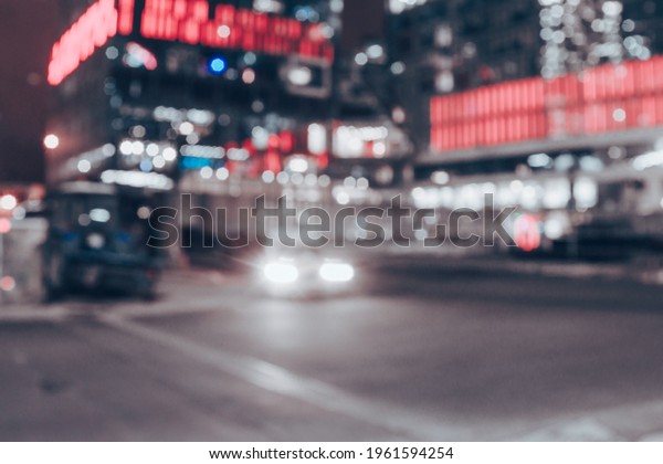 Urban night-time blurred landscape. On the way,\
cars drives and shine their headlights. There are lights behind few\
buildings. Traffic at the end of day. The concept of urban view and\
city streets.
