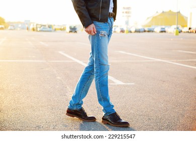 Urban outdoor fashion portrait of young stylish hipster man wearing leather biker jacket denim pants and vintage shoes posing at countryside parking evening sunlight.  - Powered by Shutterstock