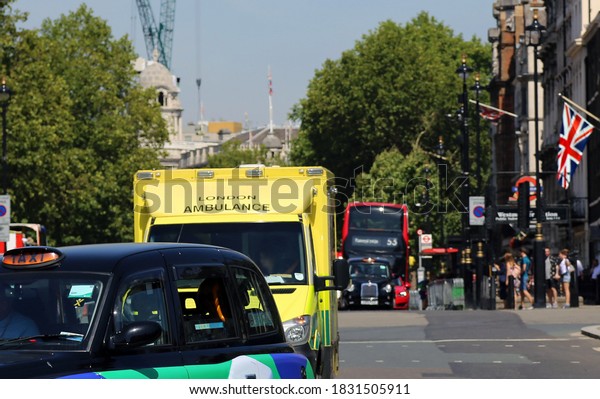 Urban perspective along a busy street in central\
London with taxi, yellow ambulance and red bus in the background.\
English flag at a\
building