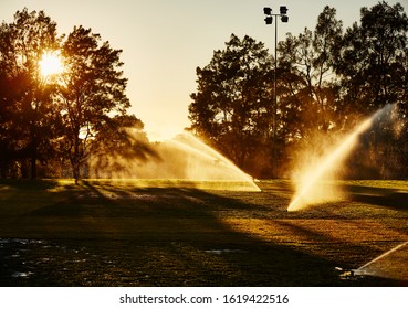 Urban Photography Of A Sunrise Over A Park Green-space Sports Oval With Sprinklers Watering The Grass