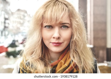 Urban portrait of a beautiful smiling Caucasian girl with blond curly hair looking at the camera
