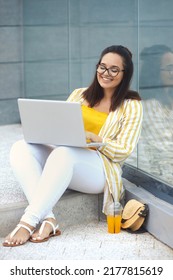 Urban Portrait Of Beautiful And Smiling Stylish Plus Size Business Woman 30-35 Years Old In Yellow Fashion Clothes And Eyeglasses, Working Remotely On A Laptop