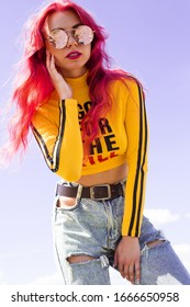 Urban Portrait Of A Girl With Red Hair, A Yellow T-shirt And Ripped Jeans, Pink Headphones, Listens To Music. 2000s Style, 2020 Trends