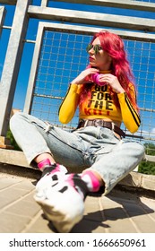 Urban Portrait Of A Girl With Red Hair, A Yellow T-shirt And Ripped Jeans, Pink Headphones, Listens To Music. 2000s Style, 2020 Trends