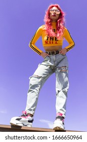 Urban Portrait Of A Girl With Red Hair, A Yellow T-shirt And Ripped Jeans, Pink Headphones, Listens To Music. 2000s Style, 2020 Trends