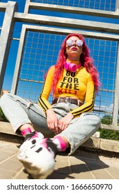 Urban Portrait Of A Girl With Red Hair, A Yellow T-shirt And Ripped Jeans, Pink Headphones, Listens To Music. 2000s Style, 2020 Trends