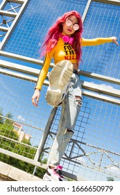 Urban Portrait Of A Girl With Red Hair, A Yellow T-shirt And Ripped Jeans, Pink Headphones, Listens To Music. 2000s Style, 2020 Trends