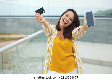 Urban Portrait Of Positive Plus Size Woman 30-35 Years Old In Fashion Clothes Doing Online Shopping With Mobile Phone And Bank Credit Card In The City Park Outdoors