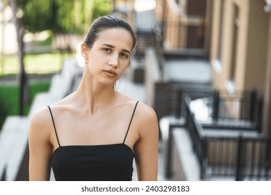 Urban portrait of a young thin woman in a black dress with open collarbones close up.