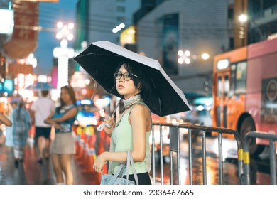 Urban real people lifestyles in downtown concept. Young asian woman wear y2k nostalgia trend outfit stylish. Using umbrella under rainy season. Standing at chinatown night market Bangkok city Thailand