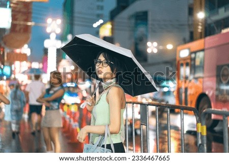 Urban real people lifestyles in downtown concept. Young asian woman wear y2k nostalgia trend outfit stylish. Using umbrella under rainy season. Standing at chinatown night market Bangkok city Thailand