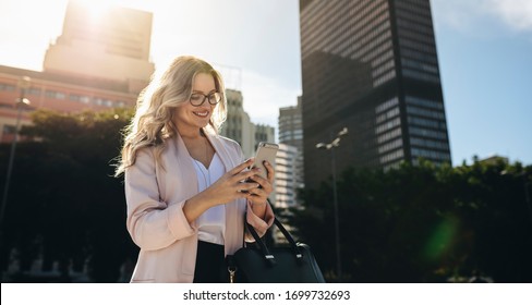 Urban realtor walking in the city using her mobile phone. Businesswoman texting on her smart phone while commuting to work. - Powered by Shutterstock