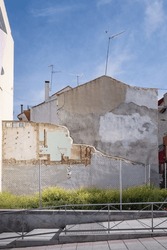 Urban Scene With An Undeveloped Plot Of Land Where The Remains Of An Old Dwelling With Light-colored Walls Can Be Seen Under A Sunny And Clear Sky.