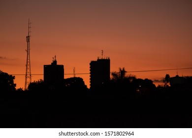 A Urban Silhouette Of A Small City Above A Orange Sky Of The Twilight